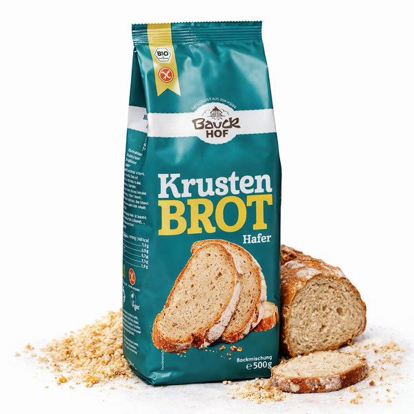 Packung bauckhof krustenbrot glutenfrei 500g vor angeschnittenem brotlaib mit brotkrümeln auf weißem Untergrund.