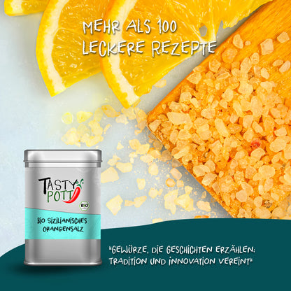 Tasty Pott Orangensalz aus Sizilien 125g Dose vor Orangenscheiben und grobem Salz, daneben Holzbrett mit Orangensalzstücken.