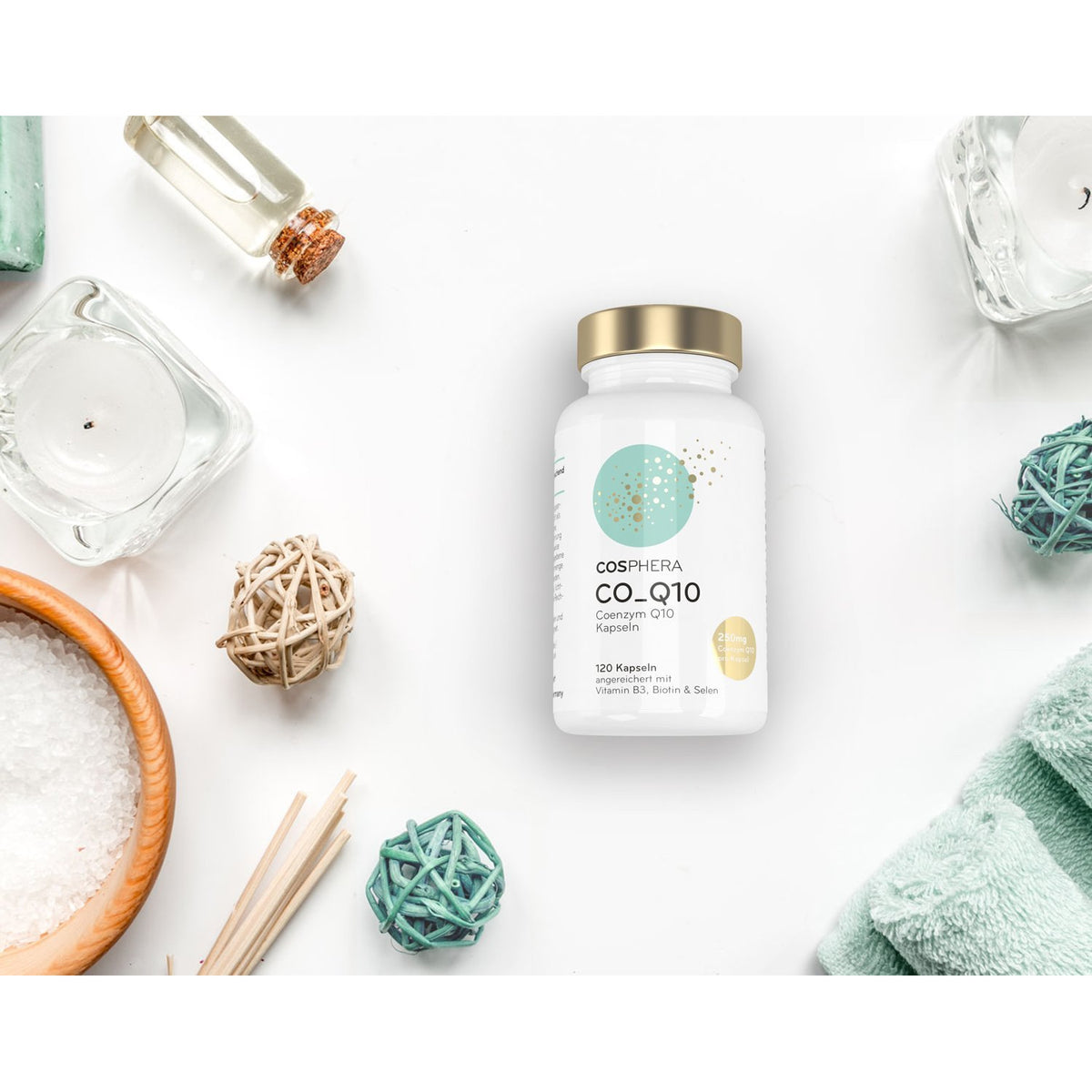 cosphera coenzym Q10 kapseln, Dose mit goldfarbenem Deckel, mittig auf weißem Hintergrund, umgeben von Wellness-Accessoires wie Handtuch, Schale mit Salz und Dekokugeln