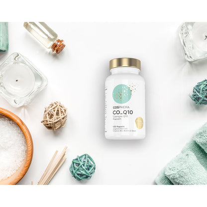 cosphera coenzym Q10 kapseln, Dose mit goldfarbenem Deckel, mittig auf weißem Hintergrund, umgeben von Wellness-Accessoires wie Handtuch, Schale mit Salz und Dekokugeln