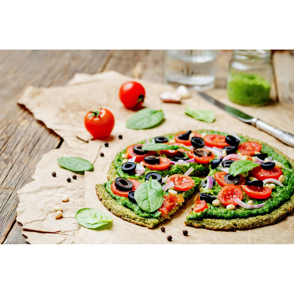 Vegetarische Pizza mit Tomaten, Oliven und Spinat auf Backpapier, ideal zum Backen mit Wohltuer Bio Produkte.