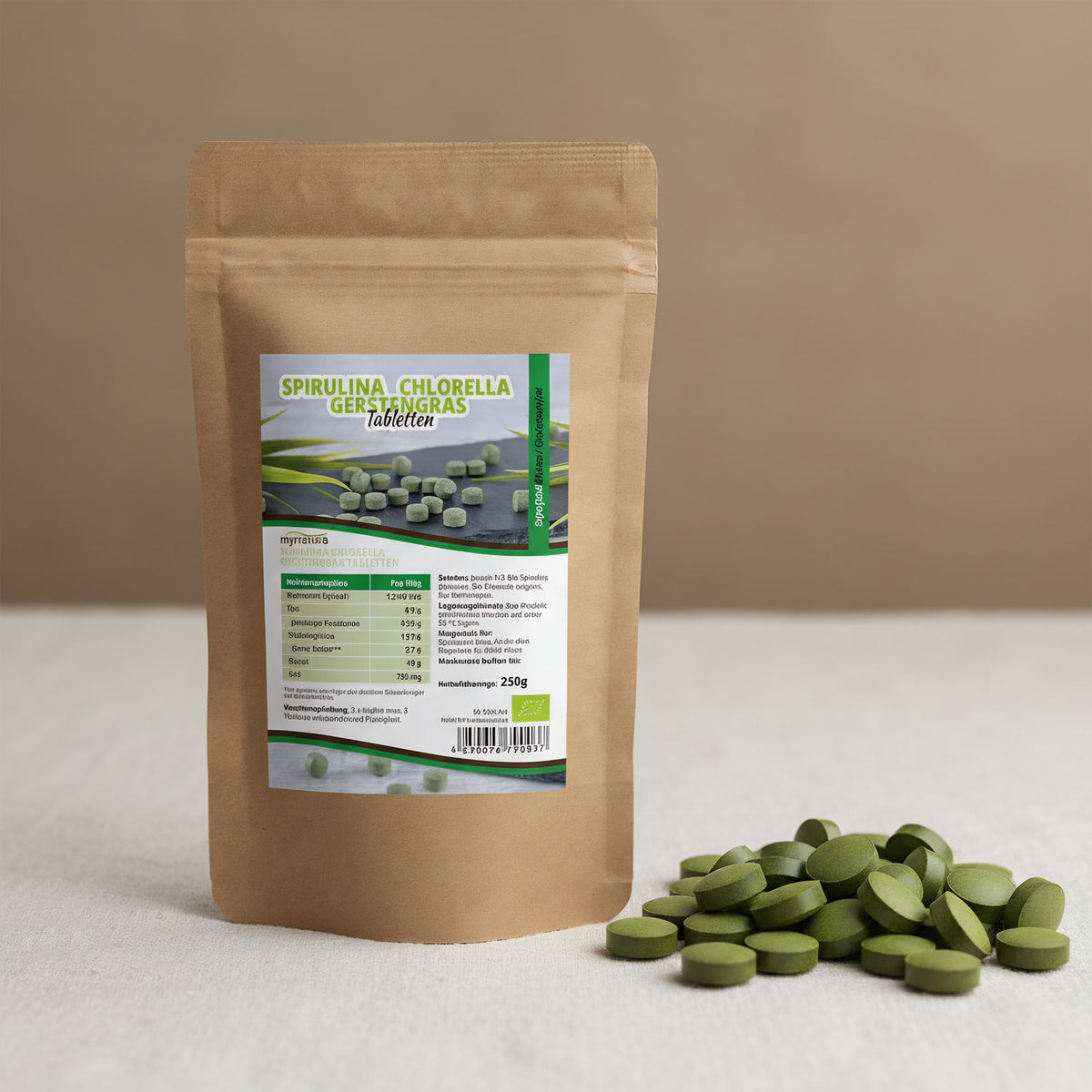 A detailed, macro-focused image showing the 'Mynatura Bio Spirulina Chlorella Gerstengras Mix Tabletten' scattered across a textured, natural fabric surface. This scene is lit with diffused daylight to bring out the rich, fresh green tones and subtle surfa