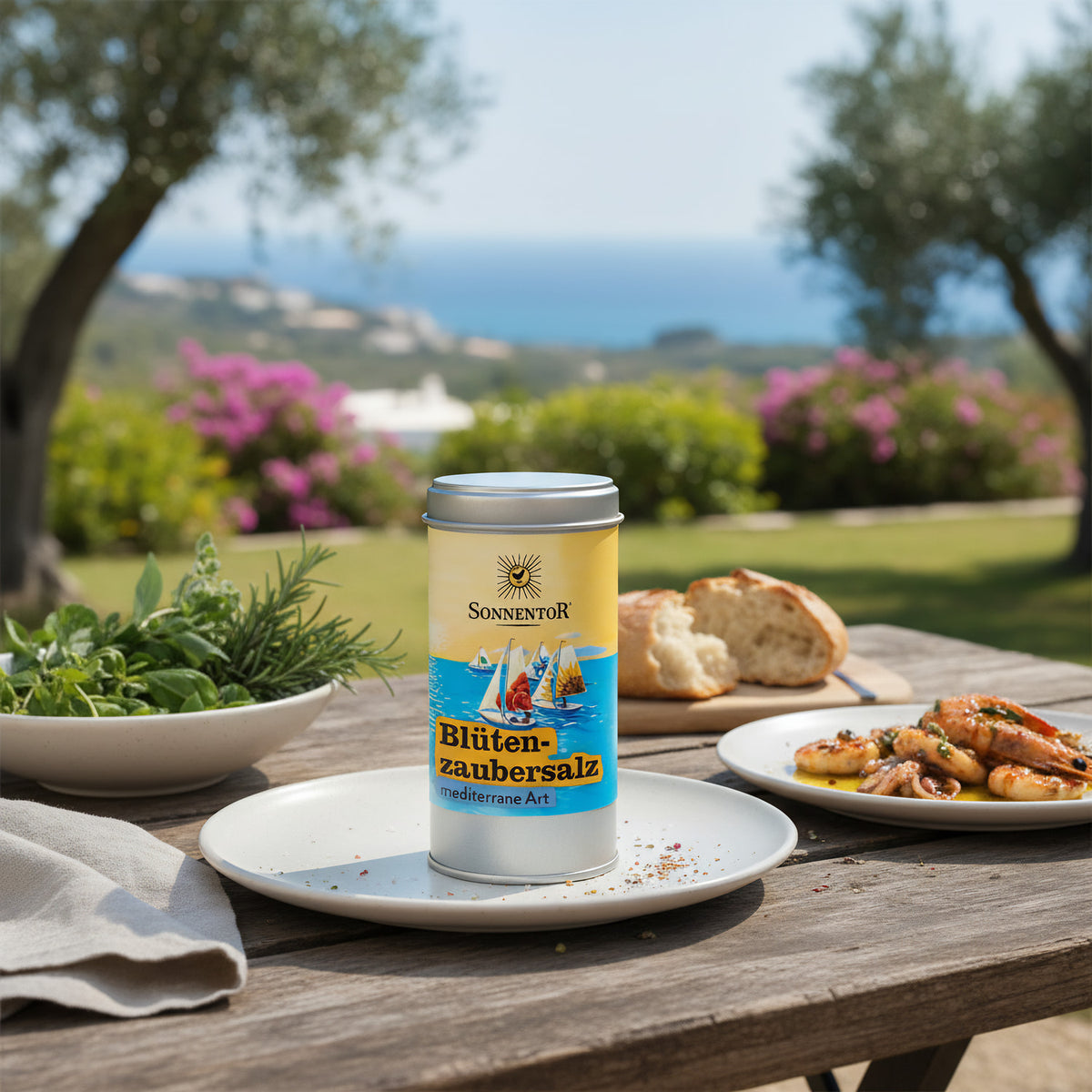 Design a lifestyle scene showing the 'Sonnentor Bio Blütenzaubersalz' jar on a rustic outdoor table set for a Mediterranean-inspired meal. Use natural diffused daylight to emphasize the warm, inviting ambiance, with the jar as the focal point, surrounded b