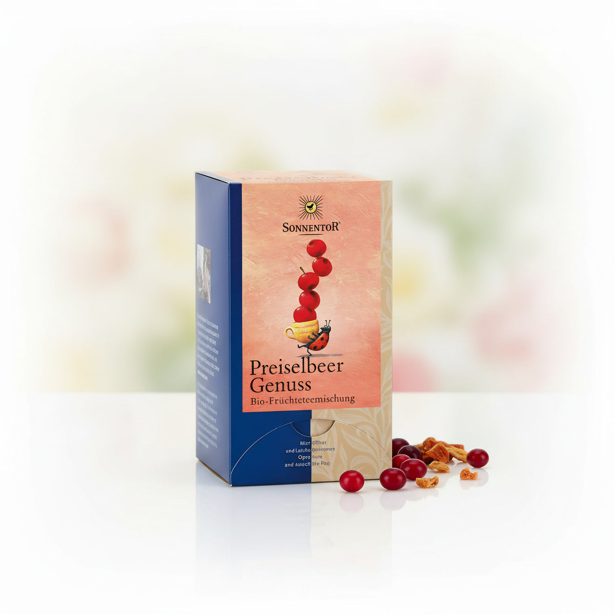 A high-resolution studio shot of the 'Sonnentor Bio Preiselbeer Genuss Früchtetee' package, shot from a slight angle to showcase the vibrant red coloration of the tea blend. The scene uses softbox lighting to create even illumination, with a subtle reflect