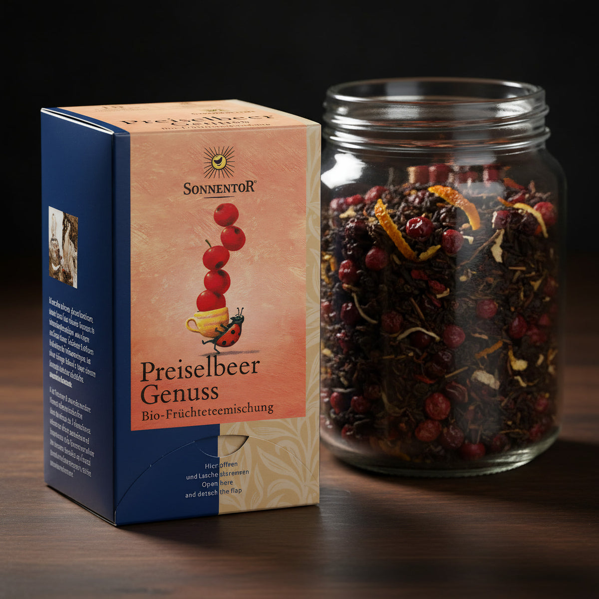 An artistic close-up shot of the tea leaves and dried Preiselbeeren in a transparent glass jar, lit with HDR studio lights to accentuate the textures and deep reds of the dried fruits and leaves. The background features a dark wooden surface that contrasts