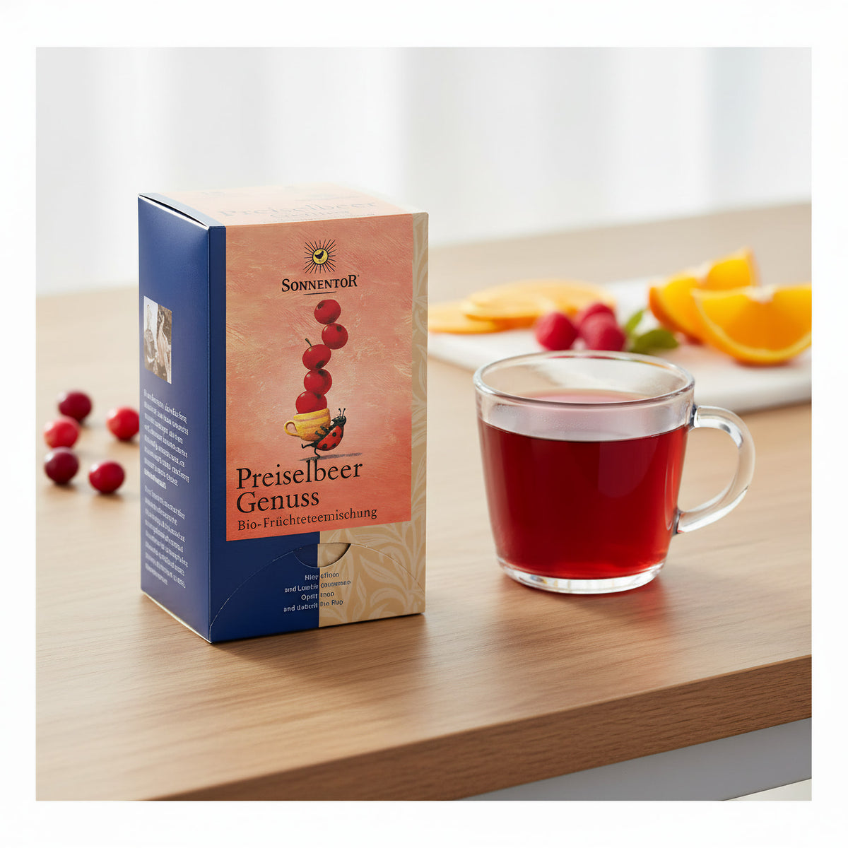 A professional product display with the Sonnentor tea box prominently centered on a sleek, modern tabletop. The setup includes a clear glass cup filled with brewed tea, showcasing the intense red hue. Backlit with diffused daylight LED lights to bring out 