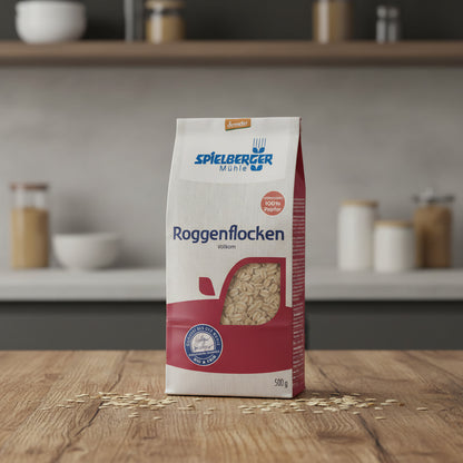 A high-resolution, studio shot of the Spielberger Bio Roggenflocken (demeter, 500g) package placed centrally on a rustic wooden table with a softbox light overhead, highlighting the natural textures of the package and the grainy surface of the flakes. The 