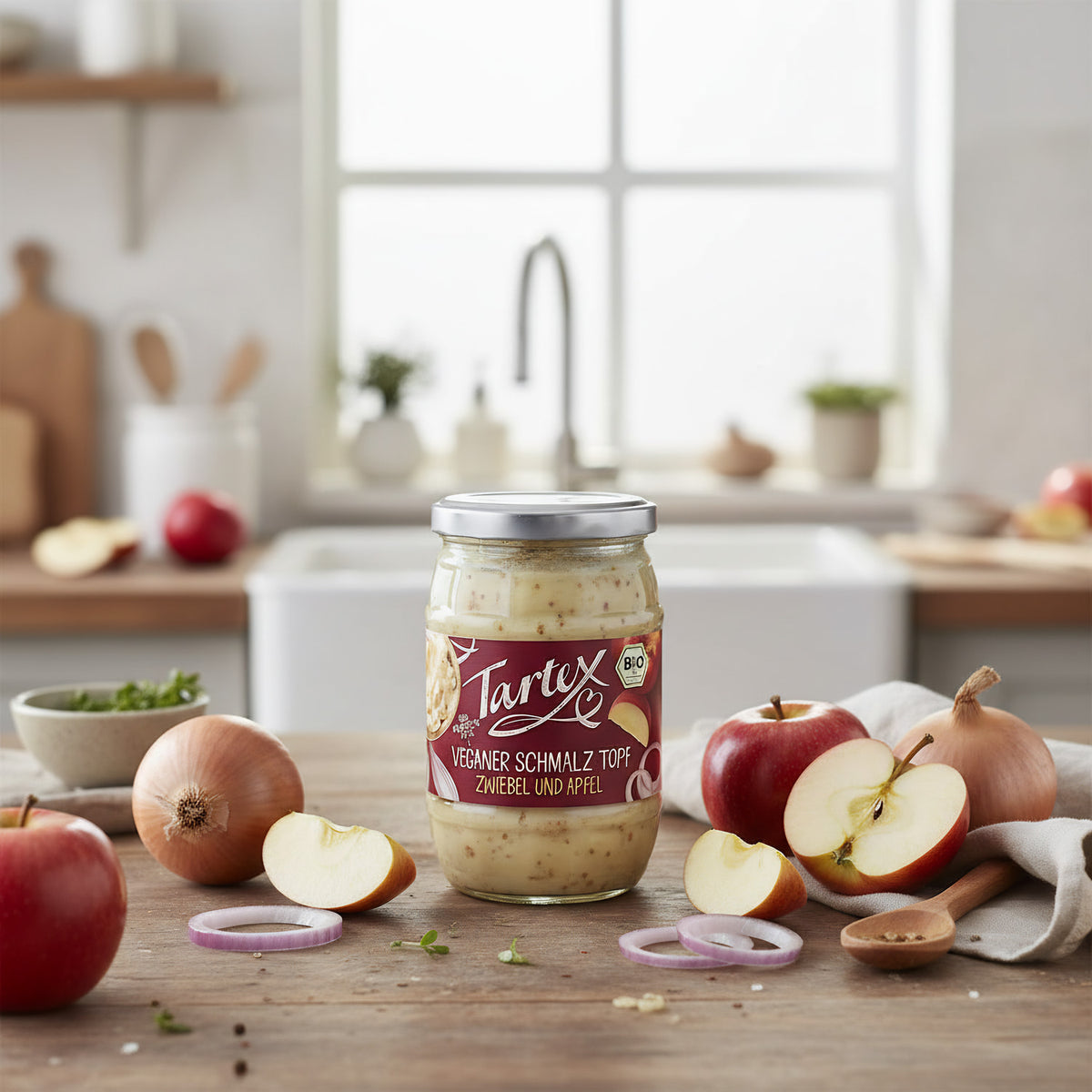 Stylish kitchen countertop display of Tartex Schmalz-Töpfle jar surrounded by fresh apples and onions, emphasizing natural ingredients and eco-friendly packaging.