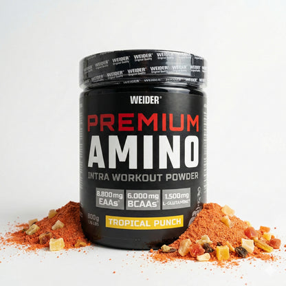 Weider Premium Amino Pulver 800g in schwarzer Dose, umgeben von orangem Pulver und getrockneten Fruchtstücken auf weißem Hintergrund.