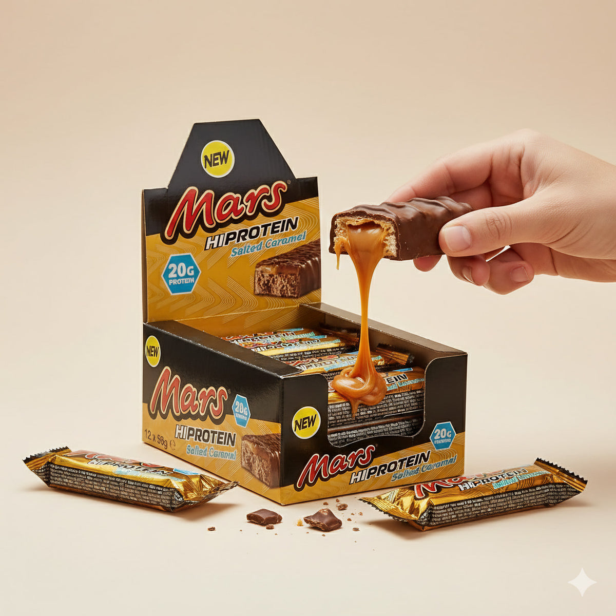 Hand hält einen halbierten Mars Proteinbar mit herauslaufendem Karamell über einer offenen Box mit weiteren Riegeln.