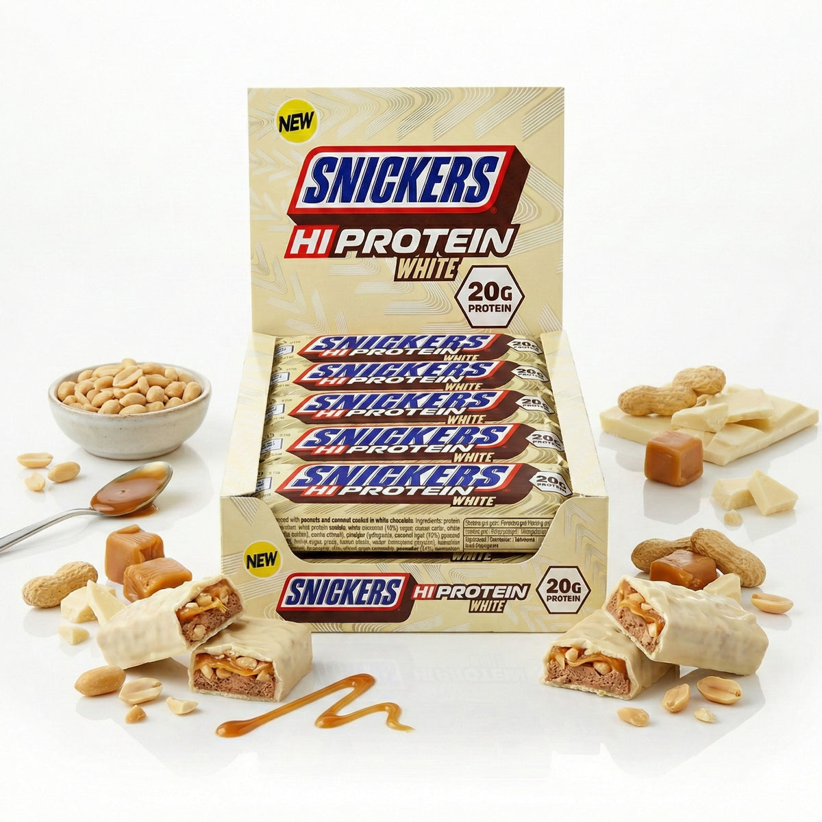 Snickers Hi-Protein White Bar 12x57g in offener Box, vorne angeschnittene weiße protein riegel, daneben Erdnüsse, weiße schokolade, Karamellwürfel und ein Löffel mit Karamell.