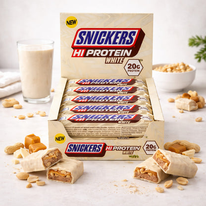 Snickers Hi-Protein White Bar 12x57g in geöffneter Verpackung, angeschnittene weiße schokoriegel im Vordergrund, im Hintergrund ein Glas Shake und Schale mit Erdnüssen.