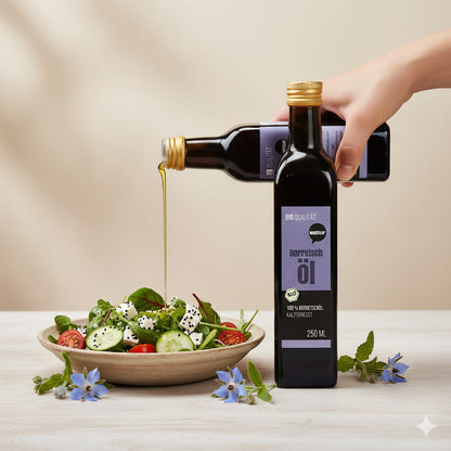 Eine Hand gießt wohltuer borretschöl nativ gepresst aus einer Flasche über einen frischen Salat mit Tomaten, Gurken und Feta, daneben Borretschblüten auf dem Tisch.