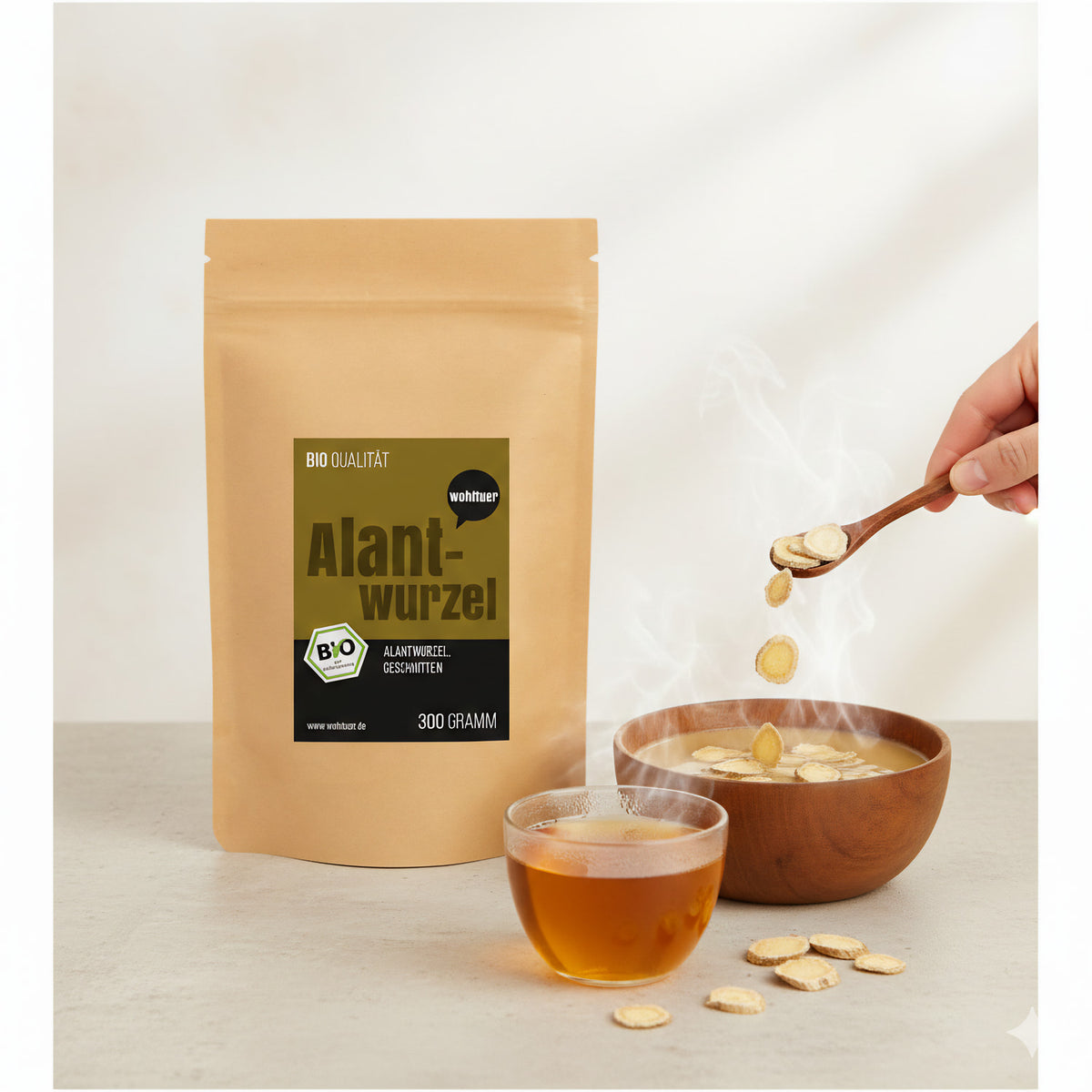 Beutel wohltuer Alantwurzel 300g neben dampfender Schale und Glas mit Kräutertee, Hand gibt getrocknete Alantwurzel-Scheiben mit Löffel hinzu.
