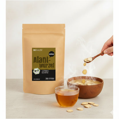 Beutel wohltuer Alantwurzel 300g neben dampfender Schale und Glas mit Kräutertee, Hand gibt getrocknete Alantwurzel-Scheiben mit Löffel hinzu.