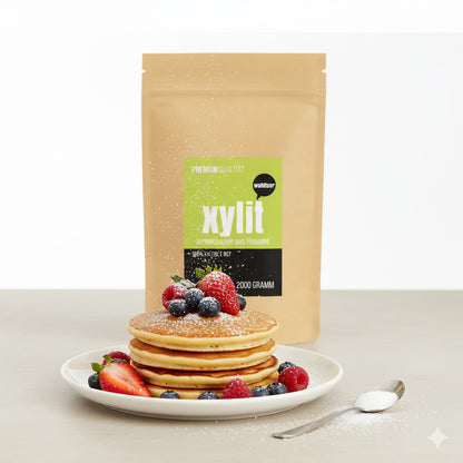 Paket wohltuer xylit birkenzucker 2000g hinter einem Teller mit Pancakes, frischen Beeren und einem Löffel Xylit, als Beispiel für Backen und Süßen.