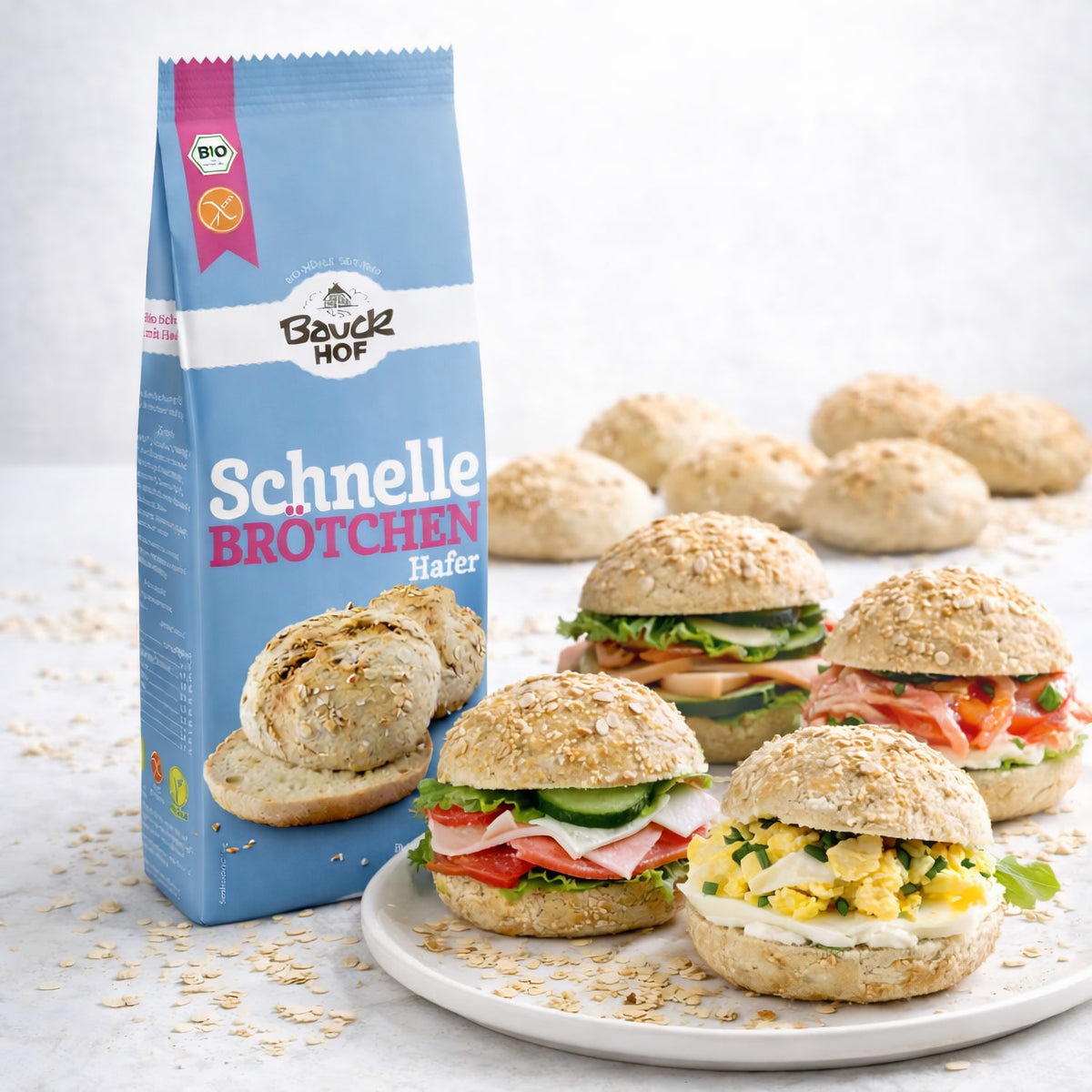 Bauckhof Schnelle Brötchen Hafer Backmischung, Packung neben einem Teller mit verschiedenen belegten glutenfreien Brötchen.