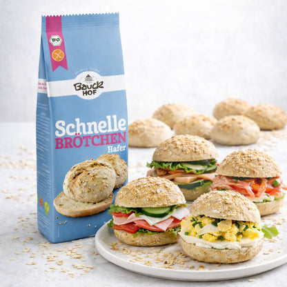 Bauckhof Schnelle Brötchen Hafer Backmischung, Packung neben einem Teller mit verschiedenen belegten glutenfreien Brötchen.