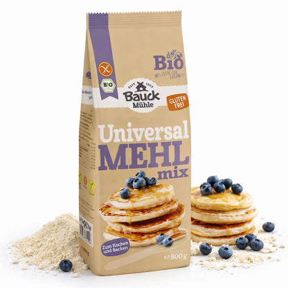 Packung Bauckhof Universal Mehl-Mix glutenfrei 800g neben einem Haufen Mehl, im Vordergrund Pancakes mit Blaubeeren auf Mehl liegend.
