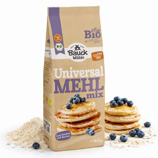 Packung Bauckhof Universal Mehl-Mix glutenfrei 800g neben einem Haufen Mehl, im Vordergrund Pancakes mit Blaubeeren auf Mehl liegend.