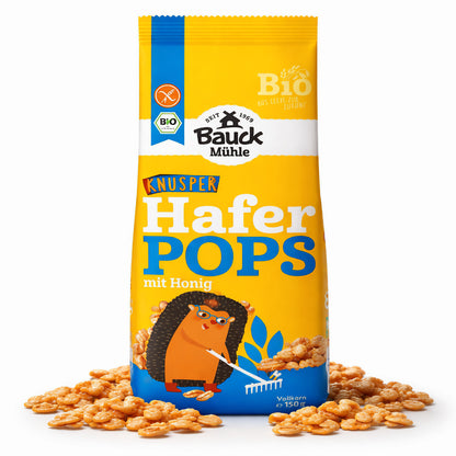 Packung Bauckhof Haferpops mit Honig, stehend auf weißem Hintergrund, umgeben von verstreuten glutenfreien Pops als Frühstücks-Snack.
