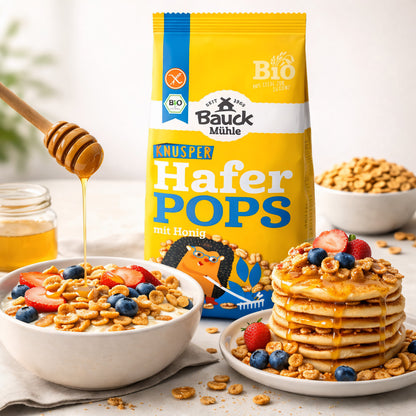 Bauckhof Haferpops mit Honig neben einer Schale Joghurt mit Pops und Pancakes, garniert mit frischen Beeren und Honig, als glutenfreies Frühstück angerichtet.