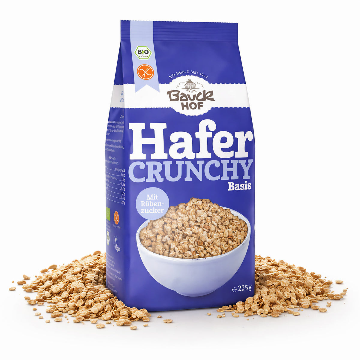 Packung Bauckhof Hafer Crunchy Basis steht aufrecht, umgeben von verstreutem Basismüsli auf weißem Hintergrund.