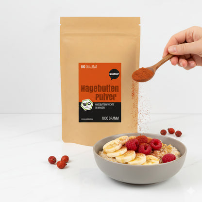 hagebuttenpulver von wohltuer neben einer Schale Porridge mit Bananen und Himbeeren, Pulver wird mit einem Löffel darüber gestreut.
