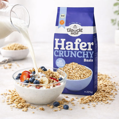 Milch wird in eine Schale mit Bauckhof Hafer Crunchy Basis, Joghurt und frischen Früchten gegossen, Verpackung steht daneben.