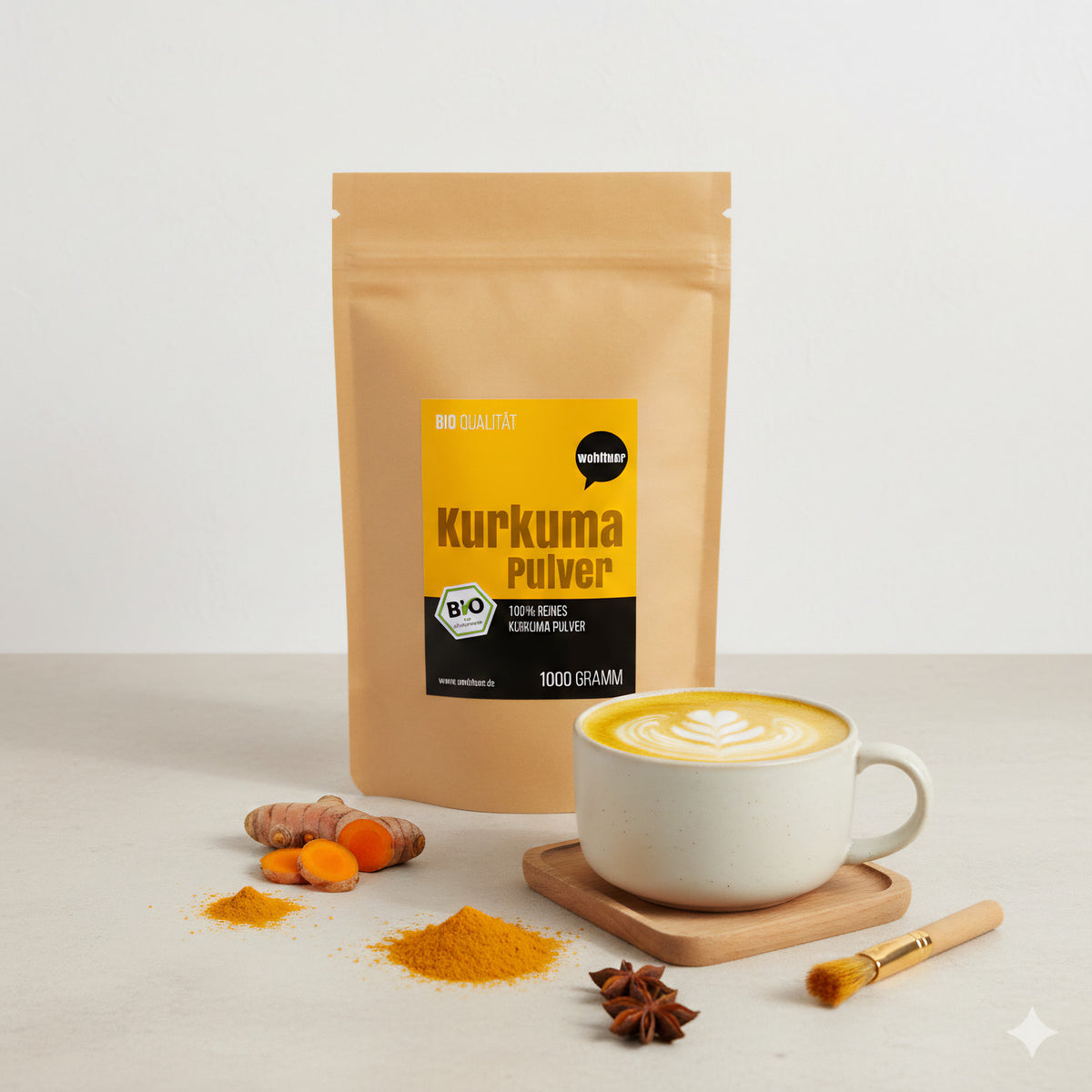 Ein wohltuer Kurkumapulver-Beutel steht neben einer Tasse Kurkuma-Latte, frischer Kurkuma-Wurzel, Pulverhäufchen und Sternanis auf hellem Tisch.