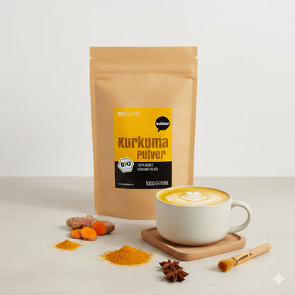 Ein wohltuer Kurkumapulver-Beutel steht neben einer Tasse Kurkuma-Latte, frischer Kurkuma-Wurzel, Pulverhäufchen und Sternanis auf hellem Tisch.