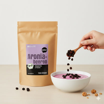 Beutel wohltuer Aroniabeeren getrocknet neben einer Schale Frühstücksjoghurt, darüber werden Früchte mit einem Löffel gestreut.