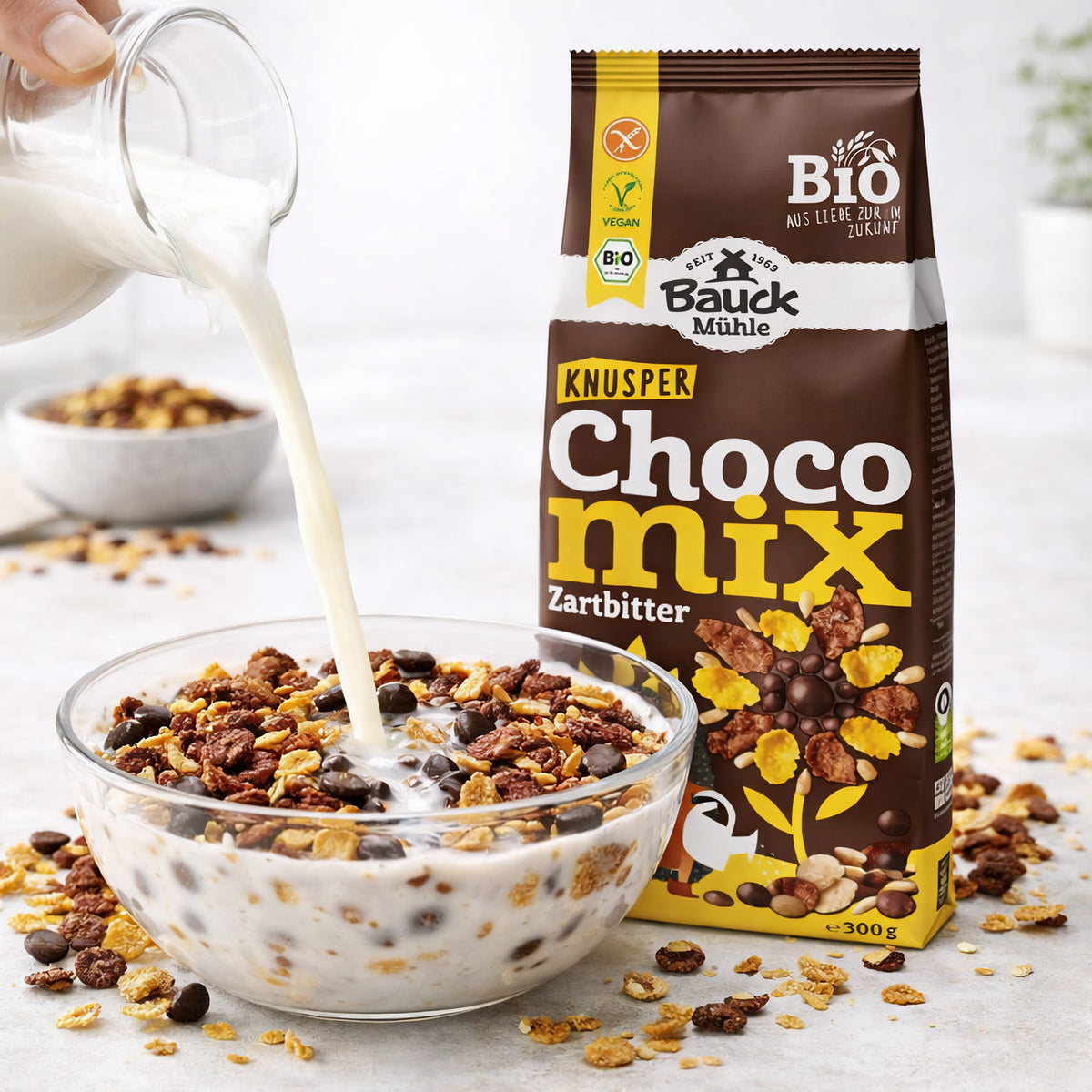 Schokomüsli von Bauck Mühle in einer Glasschale mit Milch, daneben die Packung Knusperfrühstück Zartbitter glutenfrei.