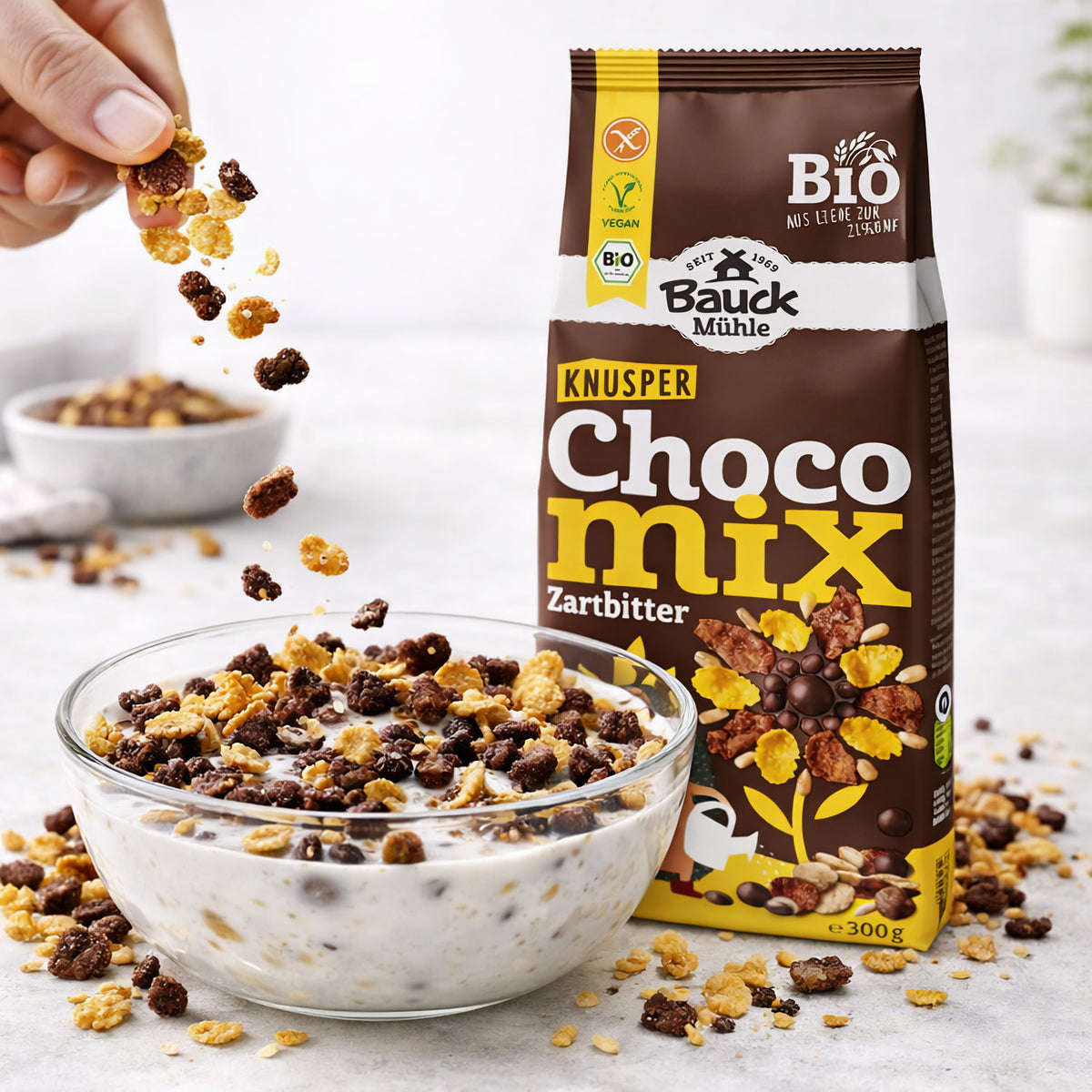 Hand streut Bauckhof Knuspermüsli Zartbitter glutenfrei in eine Schale mit Milch, Packung steht daneben.
