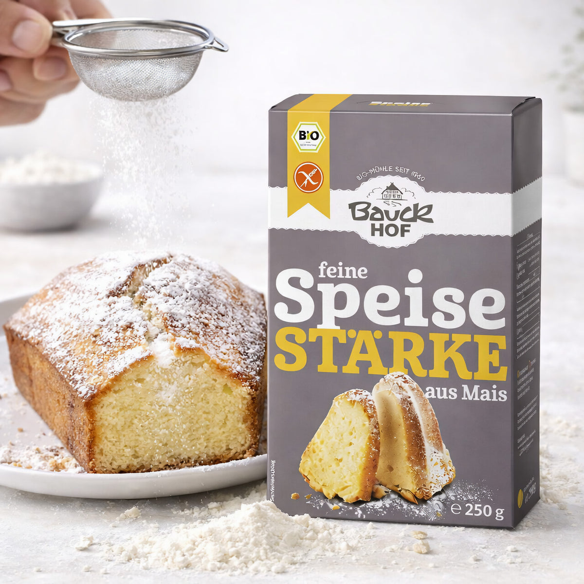 Bauckhof Speisestärke 250g neben einem Kuchen, der mit Puderzucker bestreut wird, Anwendung beim Backen