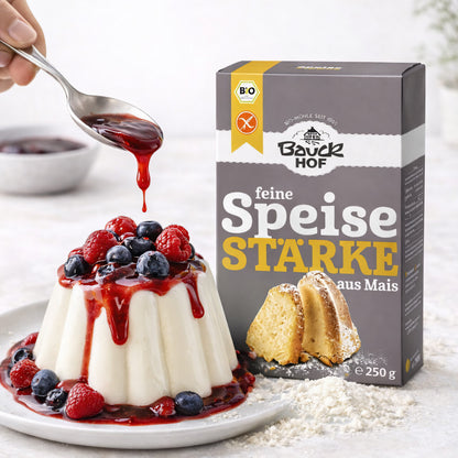 Packung Bauckhof feine Maisstärke 250g neben einem Pudding mit Beeren und roter Sauce, Verwendung beim Kochen von Desserts