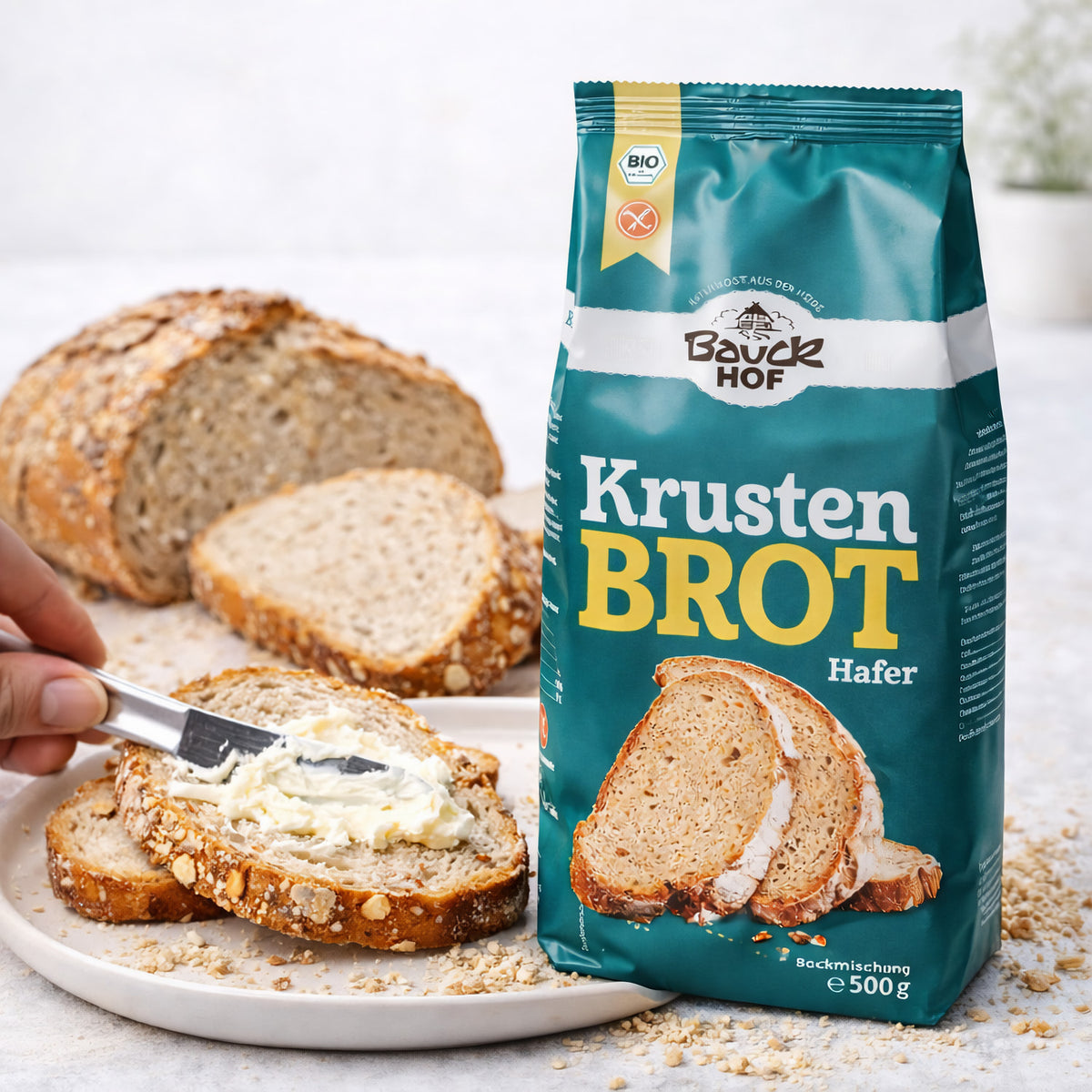 bauckhof krustenbrot glutenfrei 500g neben brotscheiben, eine scheibe wird mit butter bestrichen.