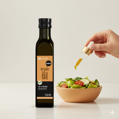 Eine Flasche wohltuer Arganöl nativ gepresst neben einer Hand, die mit einer Pipette etwas Öl über einen frischen Salat in einer Holzschale träufelt.