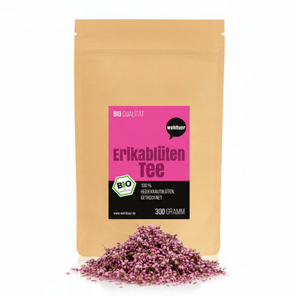 Beutel wohltuer Bio ErikablütenTee gerebelt 300g mit losem Haufen getrockneter Erikablüten davor auf weißem Hintergrund.