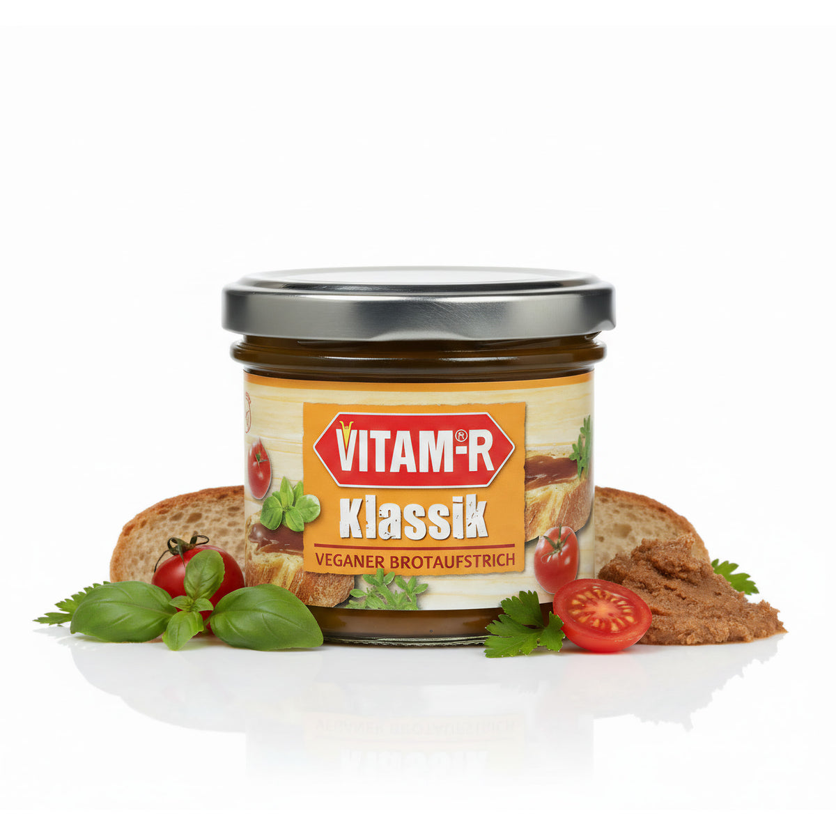 Glas VITAM-R Hefeextrakt Brotaufstrich 125g vor Brotscheiben, Tomaten, Basilikum und Petersilie auf weißem Hintergrund.