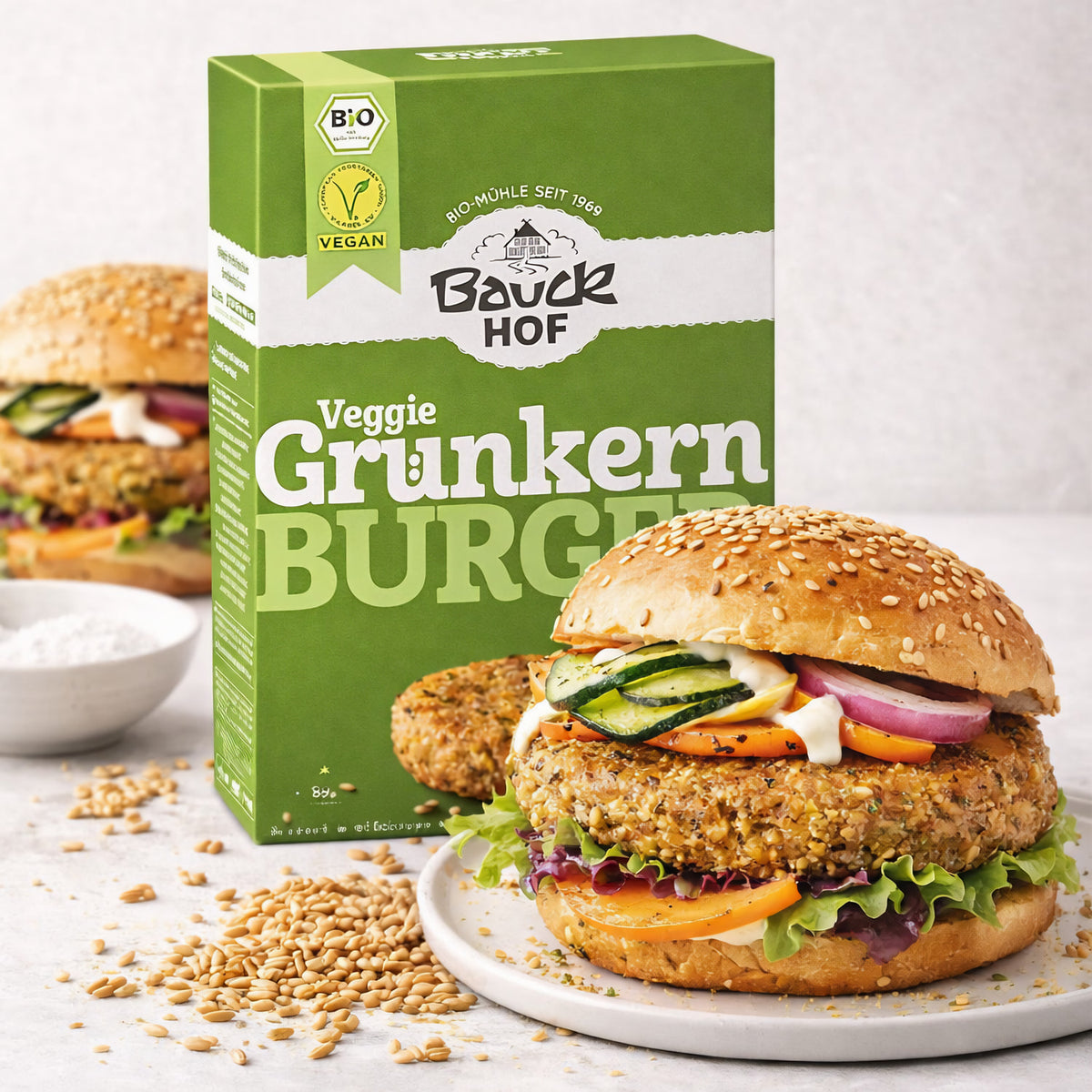 Bauckhof Grünkern-Burger Packung neben einem angerichteten vegane Burger im Sesambrötchen mit Salat, Gemüse und Grünkern-Pattie.