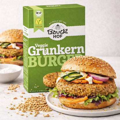 Bauckhof Grünkern-Burger Packung neben einem angerichteten vegane Burger im Sesambrötchen mit Salat, Gemüse und Grünkern-Pattie.