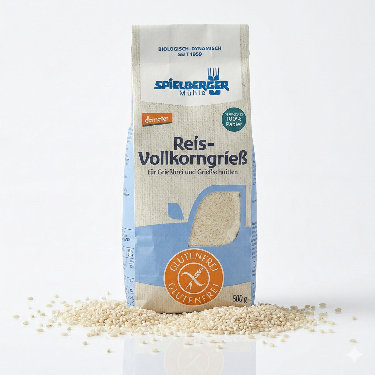 Packung spielberger glutenfreier Reis-Vollkorngrieß auf weißem Hintergrund, umgeben von verstreutem Reis, Vorderseite mit Produktinformationen sichtbar.