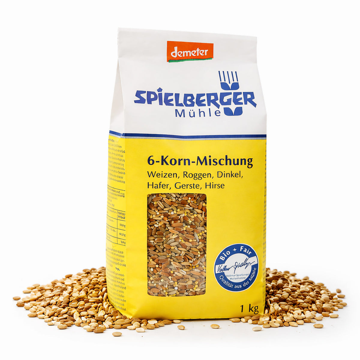 Packung Spielberger Demeter 6-Korn-Mischung 1000g stehend, umgeben von verstreuten Körnern, Vorderseite mit Sichtfenster und gelbem Etikett sichtbar.