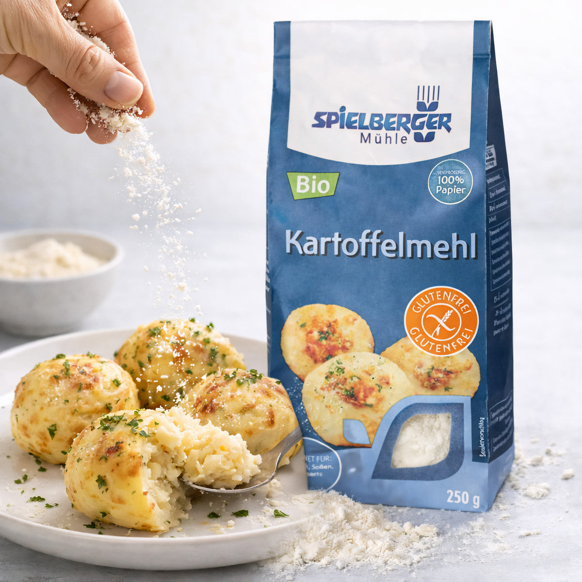 kartoffelmehl von spielberger neben angerichteten Kartoffelklößen, Hand streut mehl darüber, im Hintergrund eine Schale mit mehl