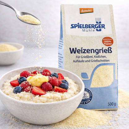 Eine Schale Grießbrei mit frischen Beeren und Butter, daneben eine Packung Spielberger Weizengrieß, im Vordergrund wird Grieß mit einem Löffel darüber gestreut.