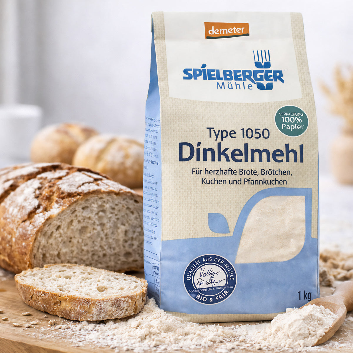Spielberger Dinkelmehl Type 1050 steht auf einem Holzbrett neben aufgeschnittenem Brot und Brötchen, mit etwas Mehl verstreut.