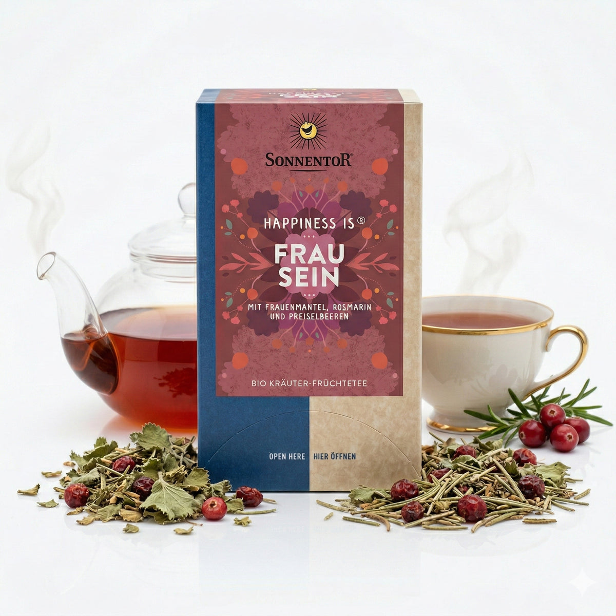 Sonnentor Frauentee Packung mit losem Kräutertee, Preiselbeeren, dampfender Teekanne und Teetasse im Hintergrund
