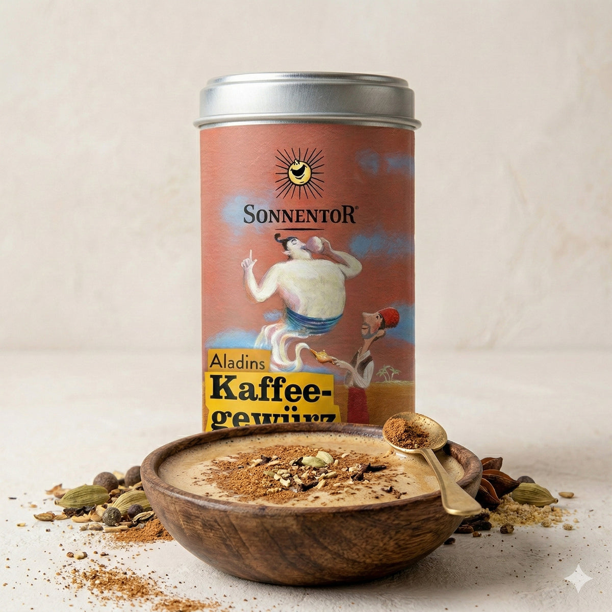 Sonnentor Aladins Kaffeegewürz Dose neben einer Holzschale mit Milchschaum und Gewürzmischung, umgeben von losen Gewürzen.