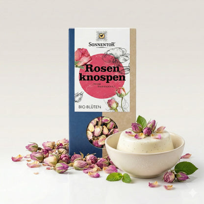 Sonnentor Bio Rosenknospen lose neben einer Schale Dessert, dekoriert mit rosenblüten und frischen Blättern.